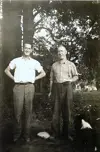 Image shows a black and white photo of two men standing under a tree. 