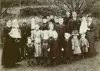 Image shows a family standing outdoors dressed in old-fashioned clothing. 