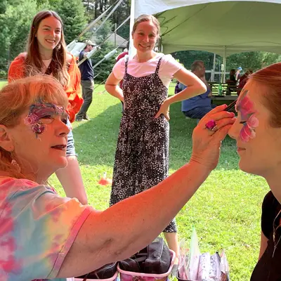 Image shows a face-painter painting a woman's face. 