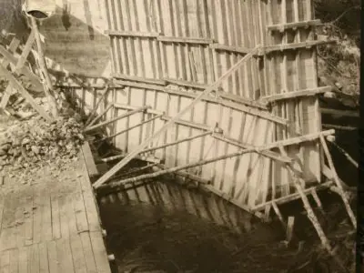 Image shows a black and white photo of the log chute under construction. 