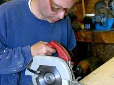 Image shows a man using a saw. 