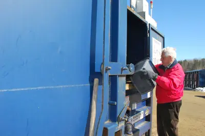 Image shows a man depositing recyclables in to a bin. 