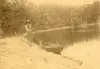 Image shows a faded photo of a person standing beside a lake. 