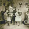 Image shows two women playing violin in a parlour. 