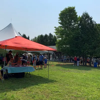 Image shows a crowd of people and event tents in a park. 