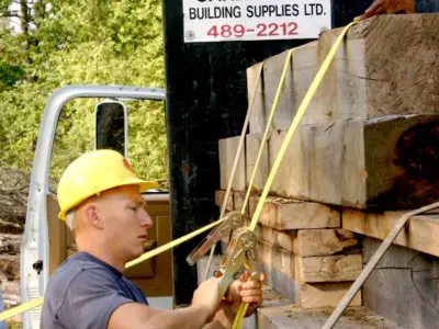 Image show a man in hardhat unloading lumber from a truck. 