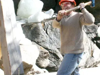 Image shows a man in a hardhat working using a sledgehammer. 