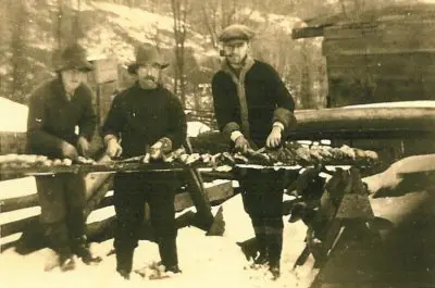 Image shows a black and white photo of three men at what appears to be a lumber camp. 