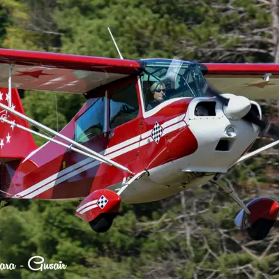 Image shows a red propeller plane in flight. 