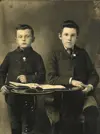 Image shows two boys in dress clothes posing with a table. 