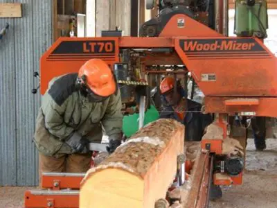 Image shows a man hewing a log. 