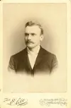 Image shows a portrait of a well-dressed man with a moustache. 