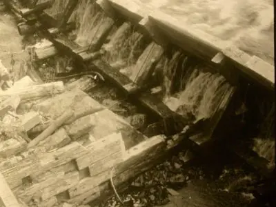 Image shows a black and white picture of the log chute with water flowing through it. 