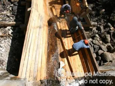 Image shows members of the construction team walking on the largely completed log chute. 